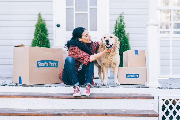Person sitting on front porch steps beside a golden retriever, surrounded by Ren&rsquo;s Pets branded shipping boxes, with a house door and greenery in the background.